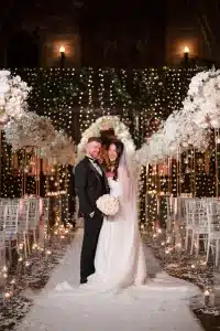 Bride and groom posing in an elegant ceremony setup at Peckforton Castle, styled with white florals and glowing candle decor by a Cheshire wedding stylist.